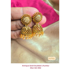 Antique gold studded jhumka earrings with kundan stones and pearl drops, handheld against pink fabric background