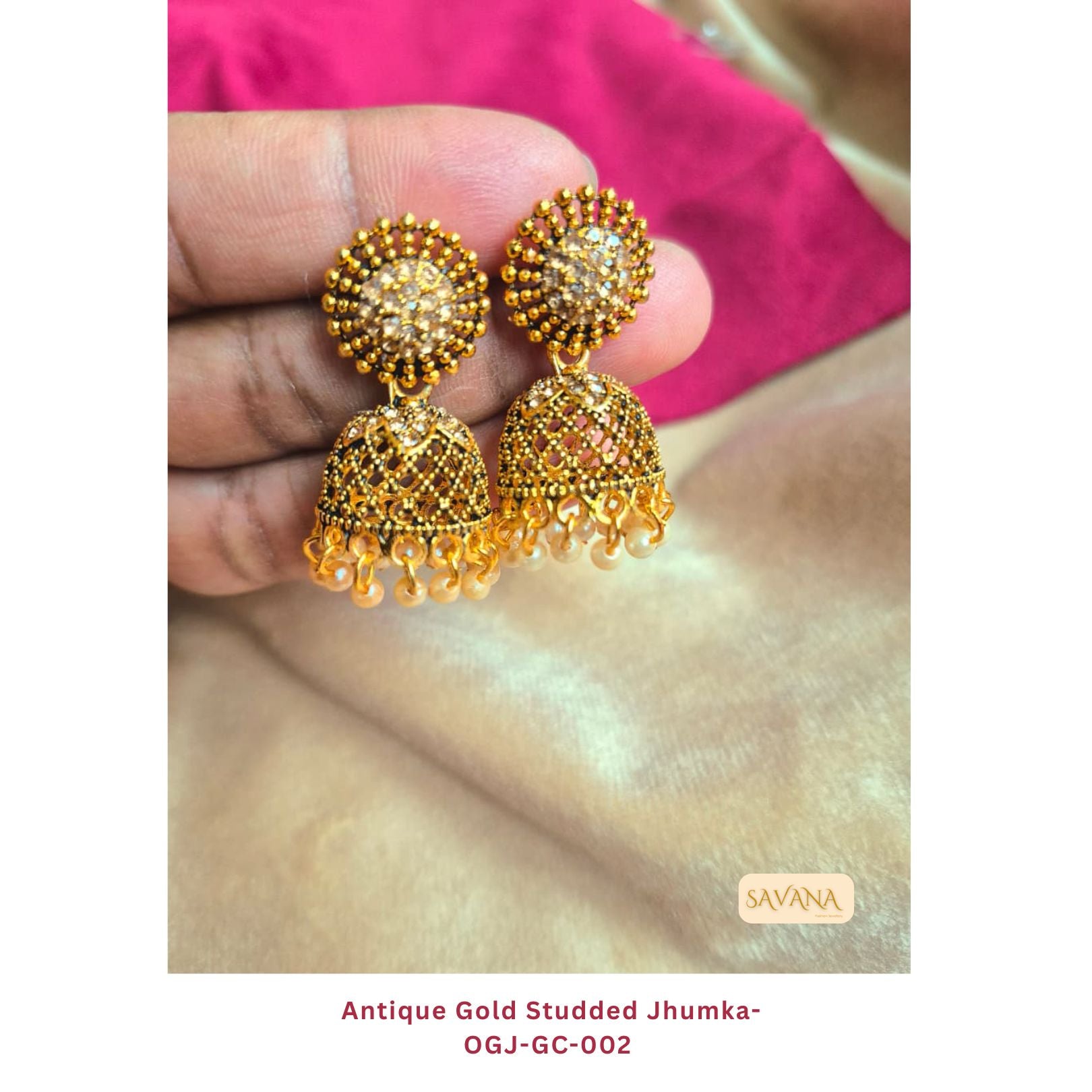 Antique gold studded jhumka earrings with kundan stones and pearl drops, handheld against pink fabric background