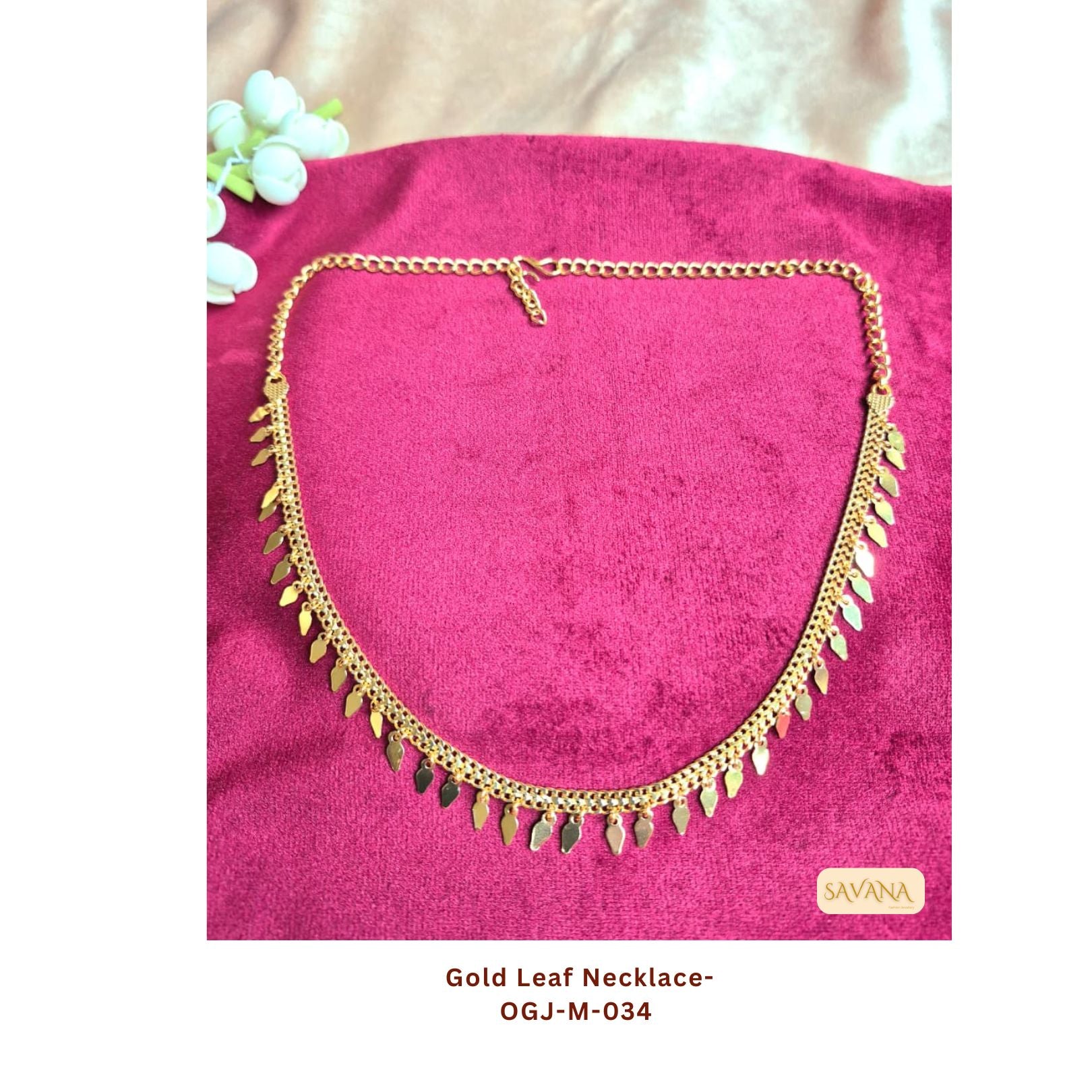 Gold plated leaf charm chain necklace laid on pink fabric background, boho ethnic style