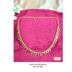Gold plated leaf charm chain necklace laid on pink fabric background, boho ethnic style